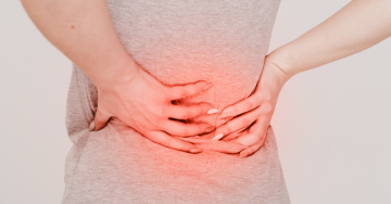 Egy nő a hát alsó részén érezhető fájdalomra mutat, amely a lumbágó jelentését és a lumbago ischiassal tüneteinek megjelenését szemlélteti.